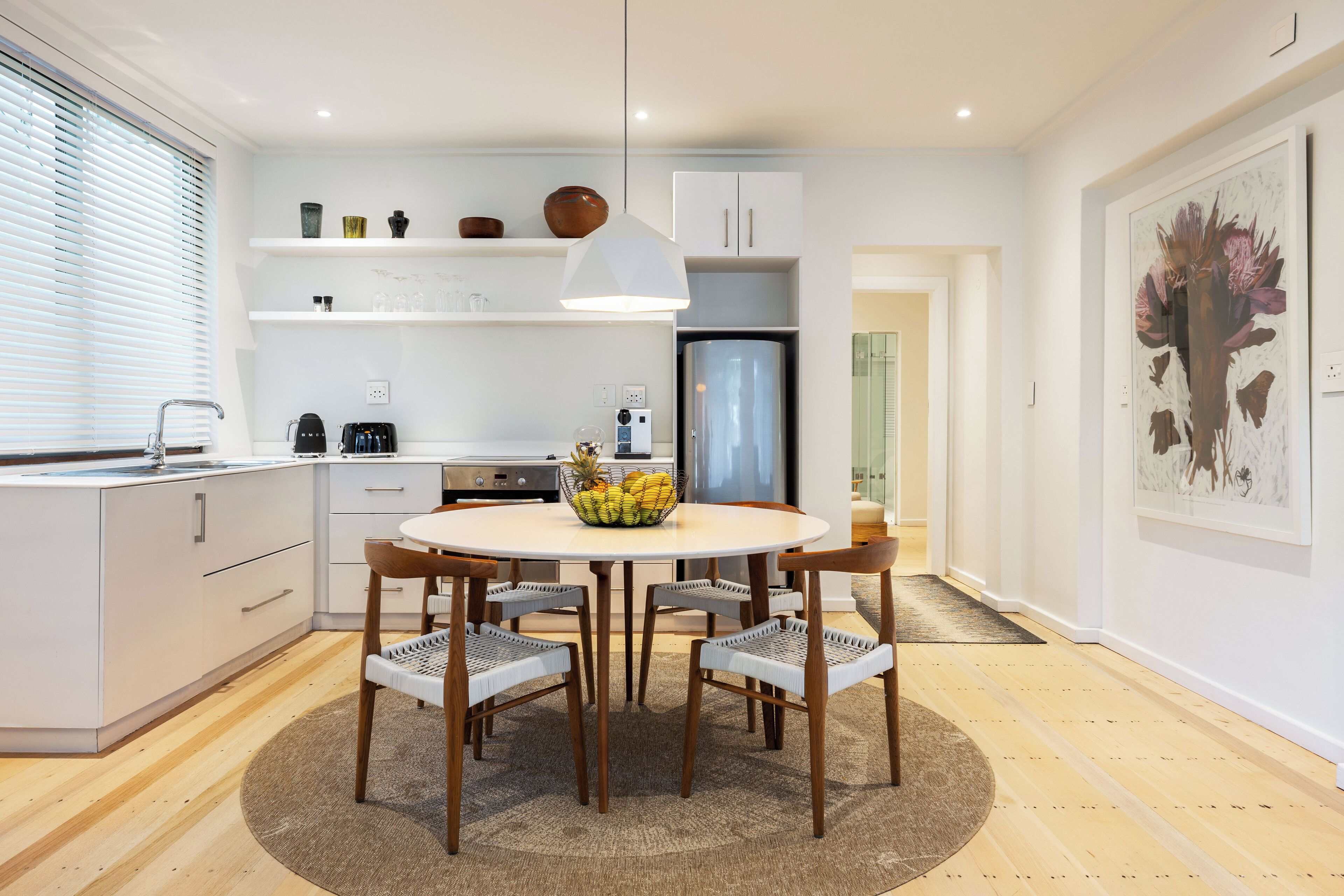 A modern kitchen with white cabinets, a round dining table, and a fruit bowl.