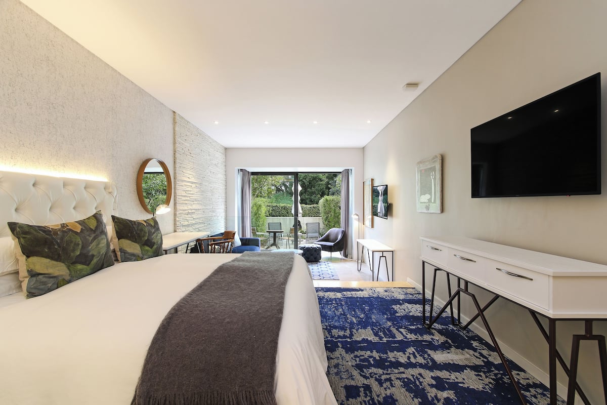 A modern hotel room with a large bed, a TV, a desk, and a view of the outdoors.