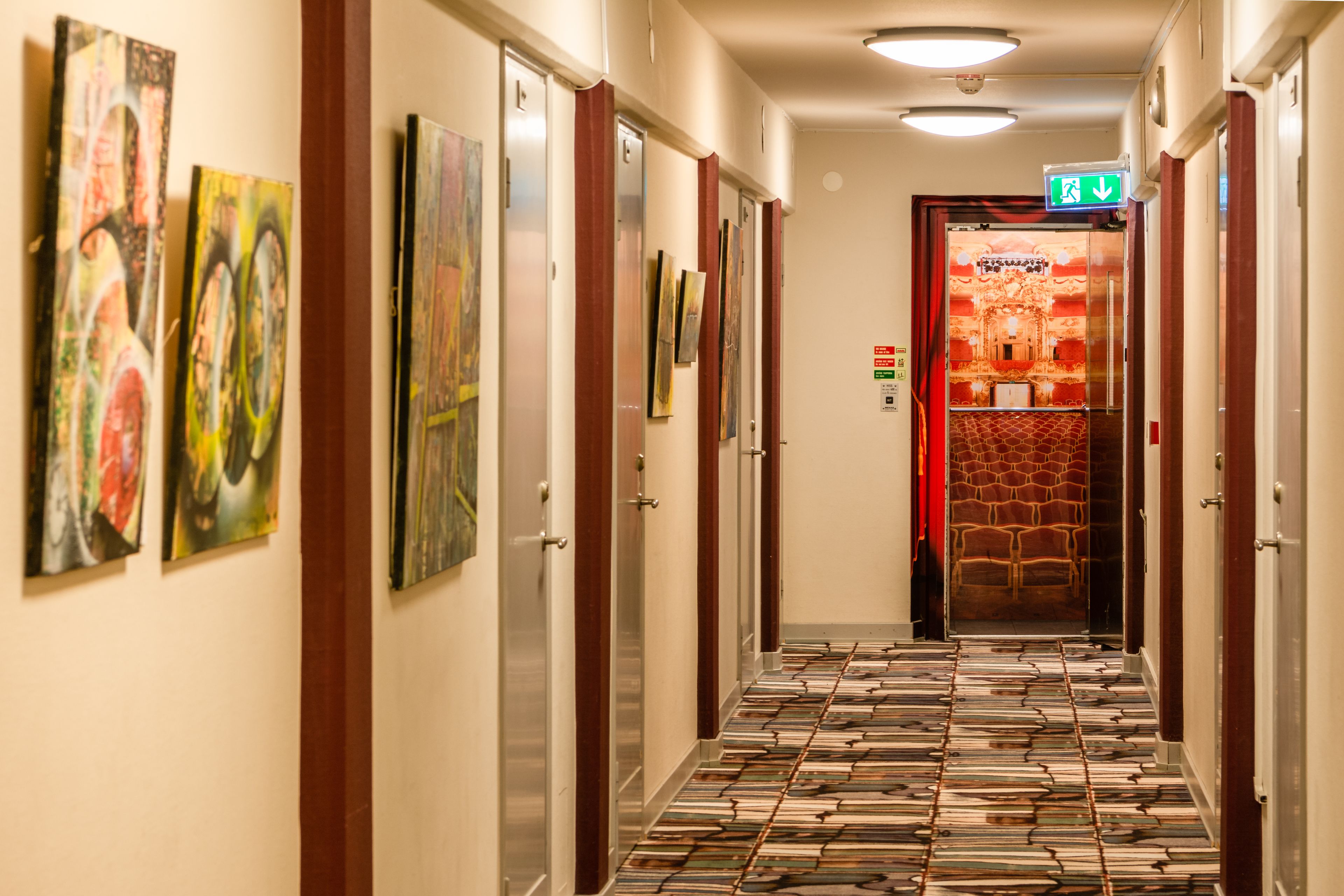 A hotel hallway with artwork on the walls, a patterned floor, and a seating area at the end.