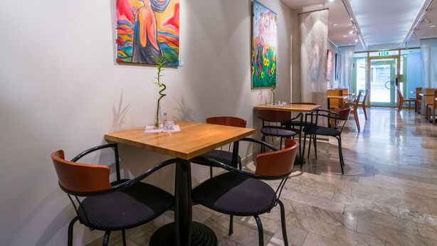 A restaurant with tables and chairs, a plant on each table, and paintings on the walls. - Teaterhotellet (Malmö)