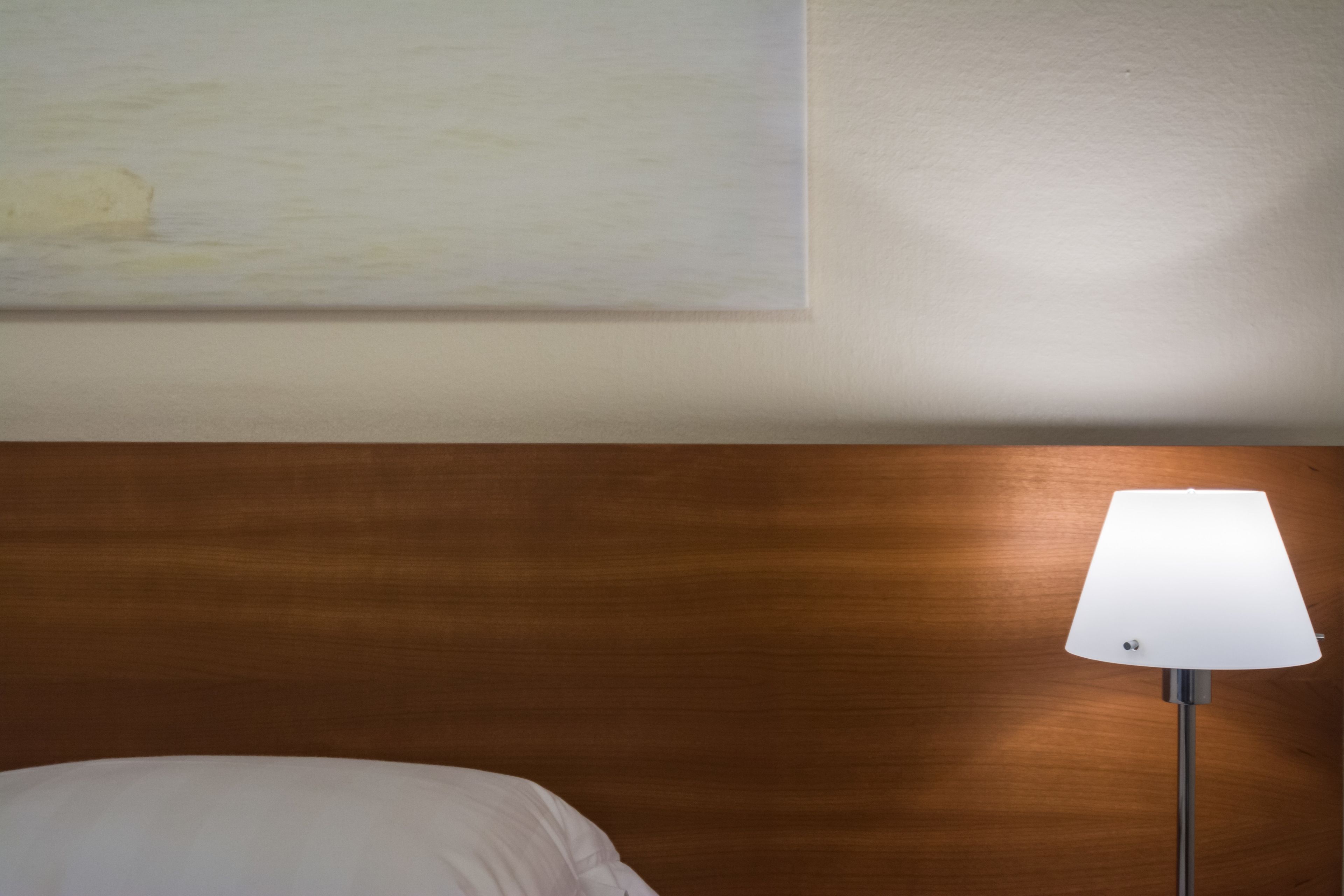 Una habitación con cabecera de madera, cama blanca y una lámpara de pie.