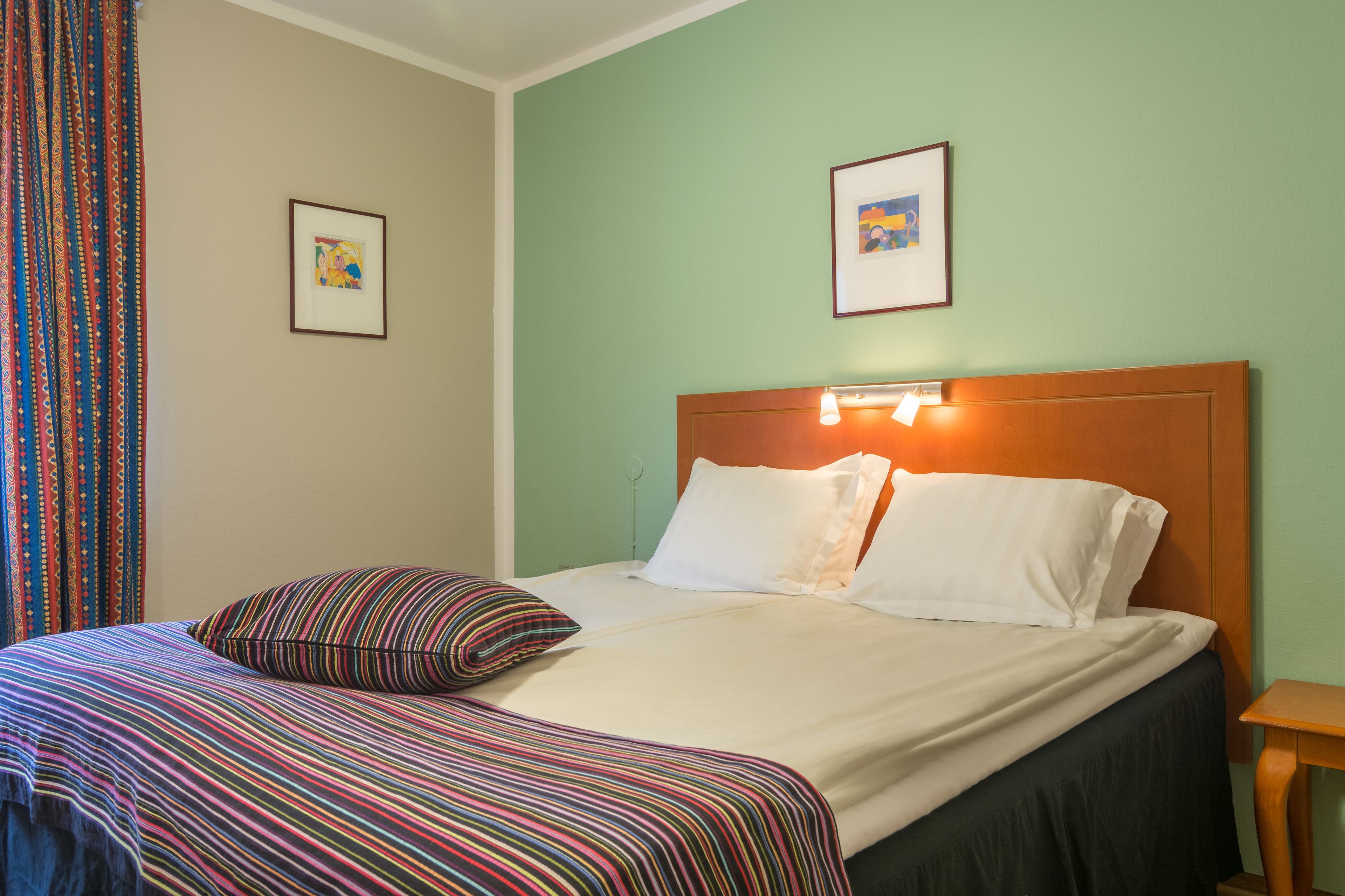 A neatly made bed with striped bedding, a wooden headboard, and two framed pictures on the wall.