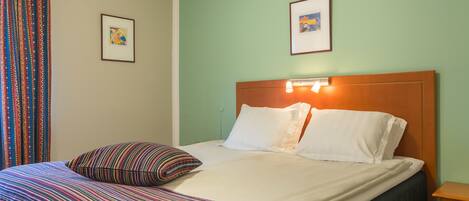 A neatly made bed with striped bedding, a wooden headboard, and two framed pictures on the wall.