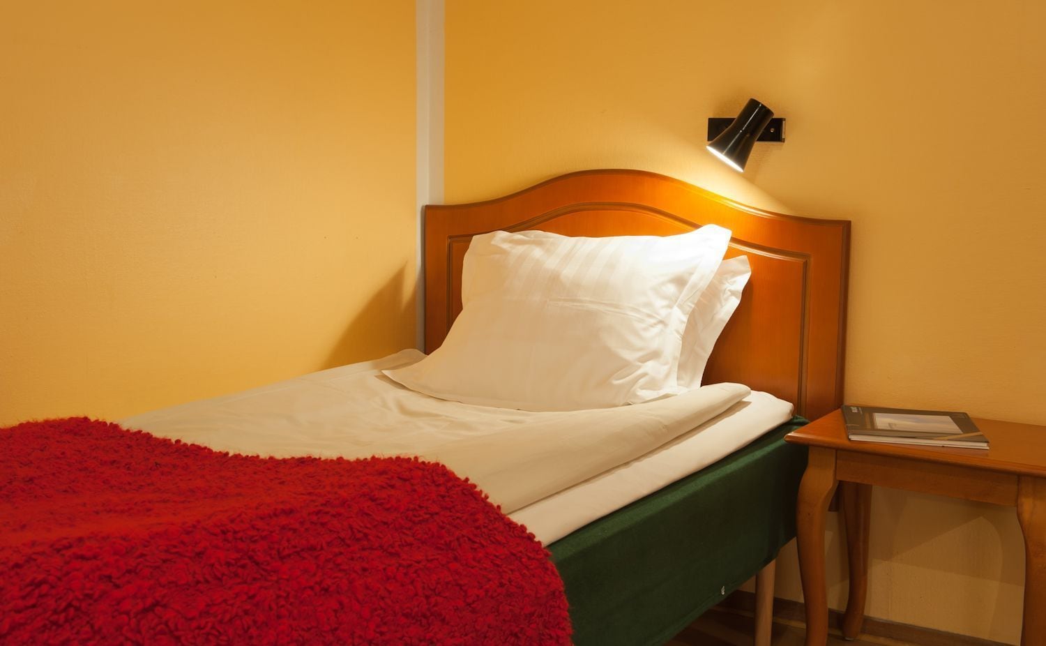 Een bed met witte beddengoed, een rode plaid en een houten hoofdbord.