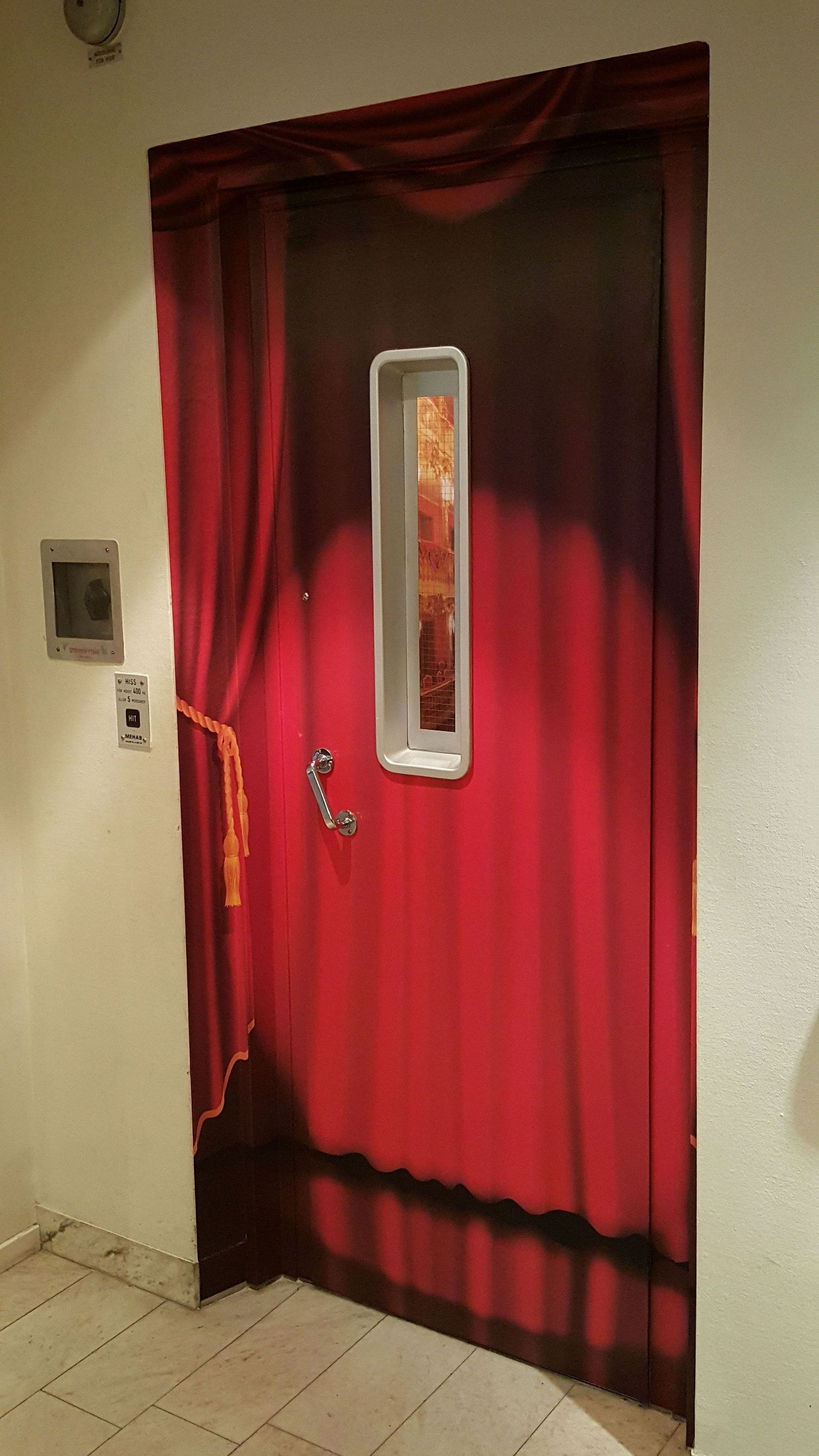 A red door with a small window, a doorbell, and a security camera.