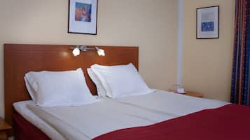 A hotel room with a wooden headboard, two white pillows, a red bedspread, and two bedside tables with lamps.