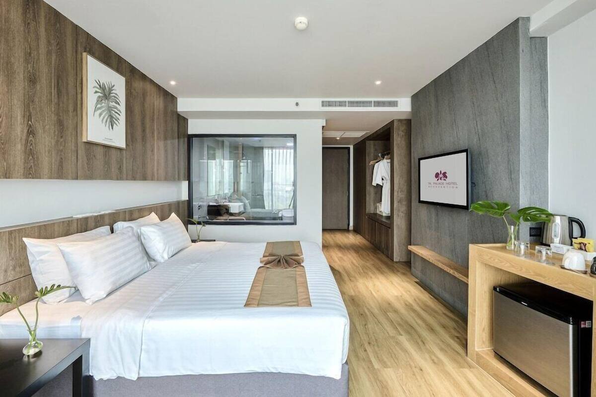 A modern hotel room with a large bed, a wooden floor, a small desk, and a view of the bathroom.
