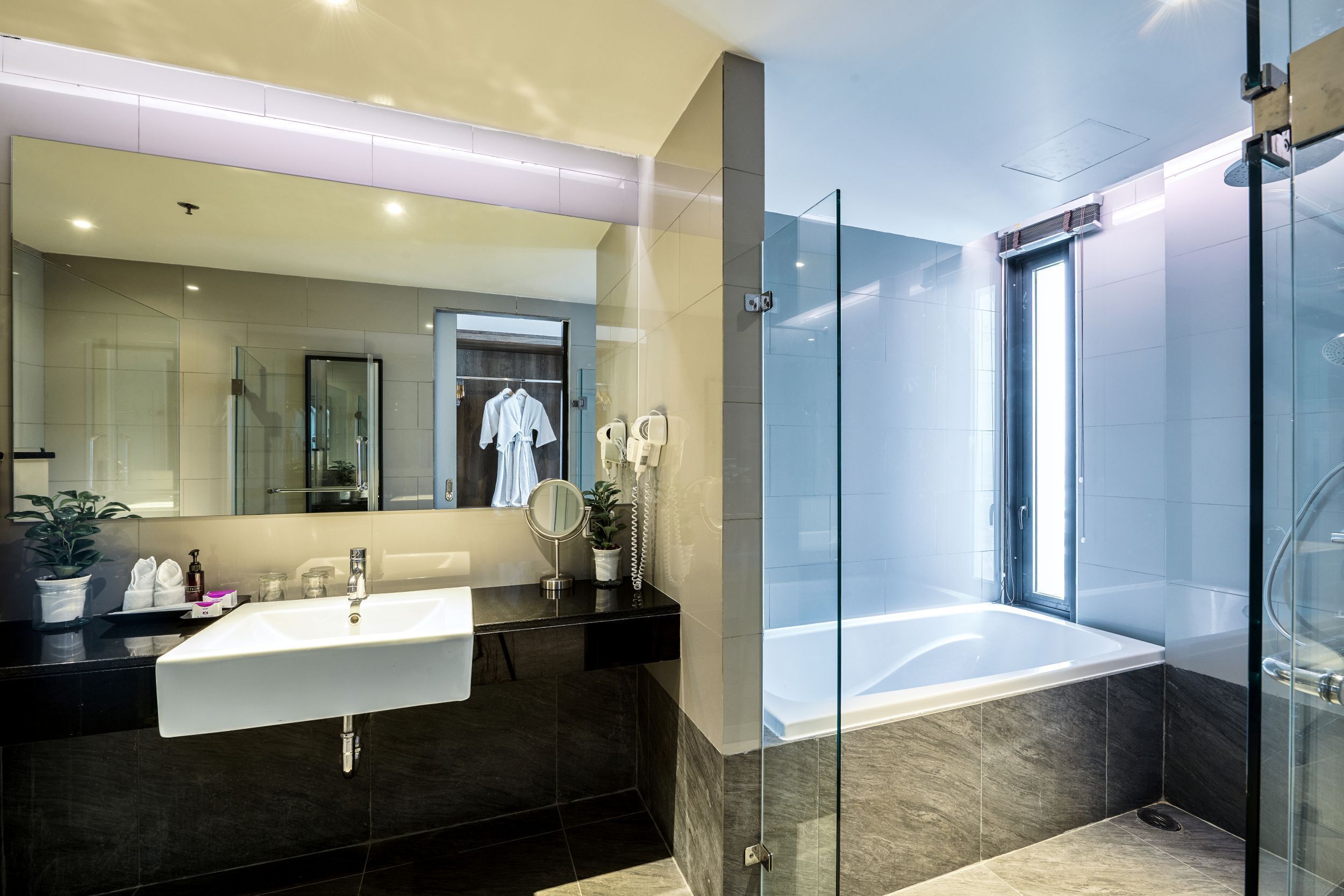 A modern bathroom with a large mirror, a white sink, a glass-enclosed shower, and a bathtub.