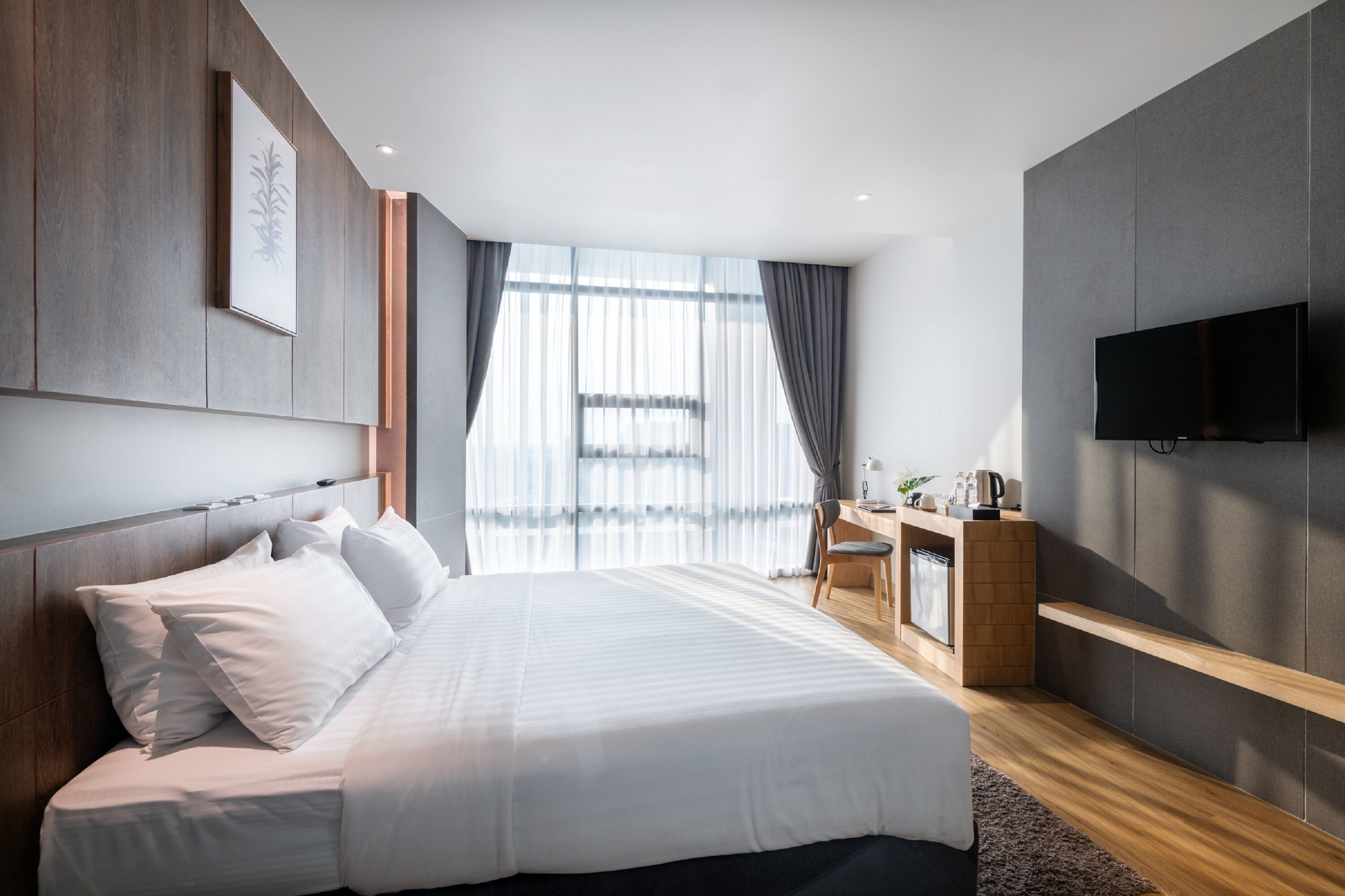 A modern hotel room with a large bed, a desk, and a TV.
