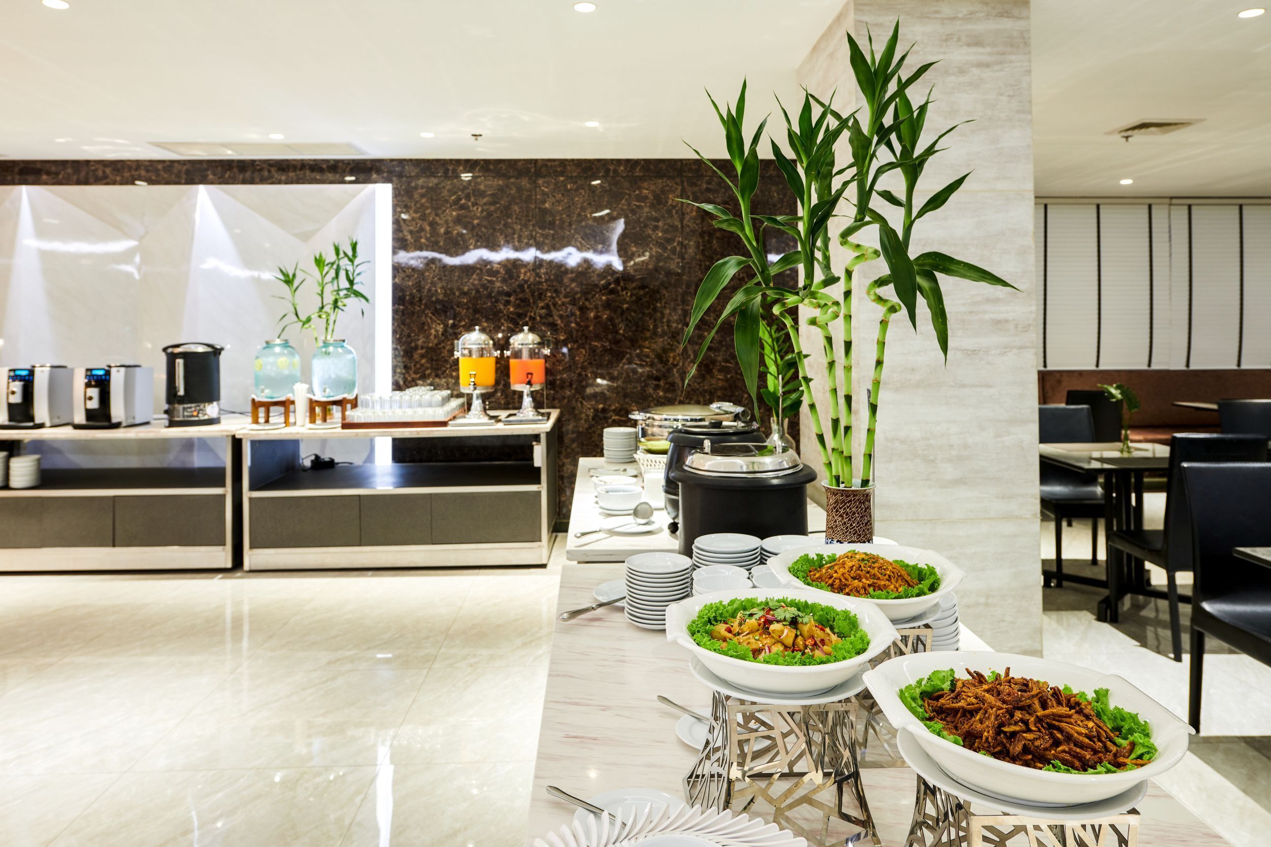 A buffet setup with various dishes, a coffee station, and a decorative bamboo plant.