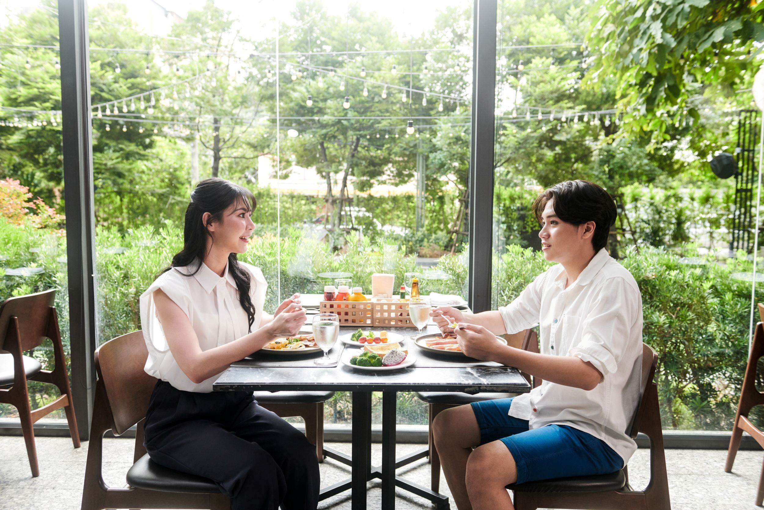 A dining table with plates of food, glasses, and a bottle, set in a room with large windows and chairs.