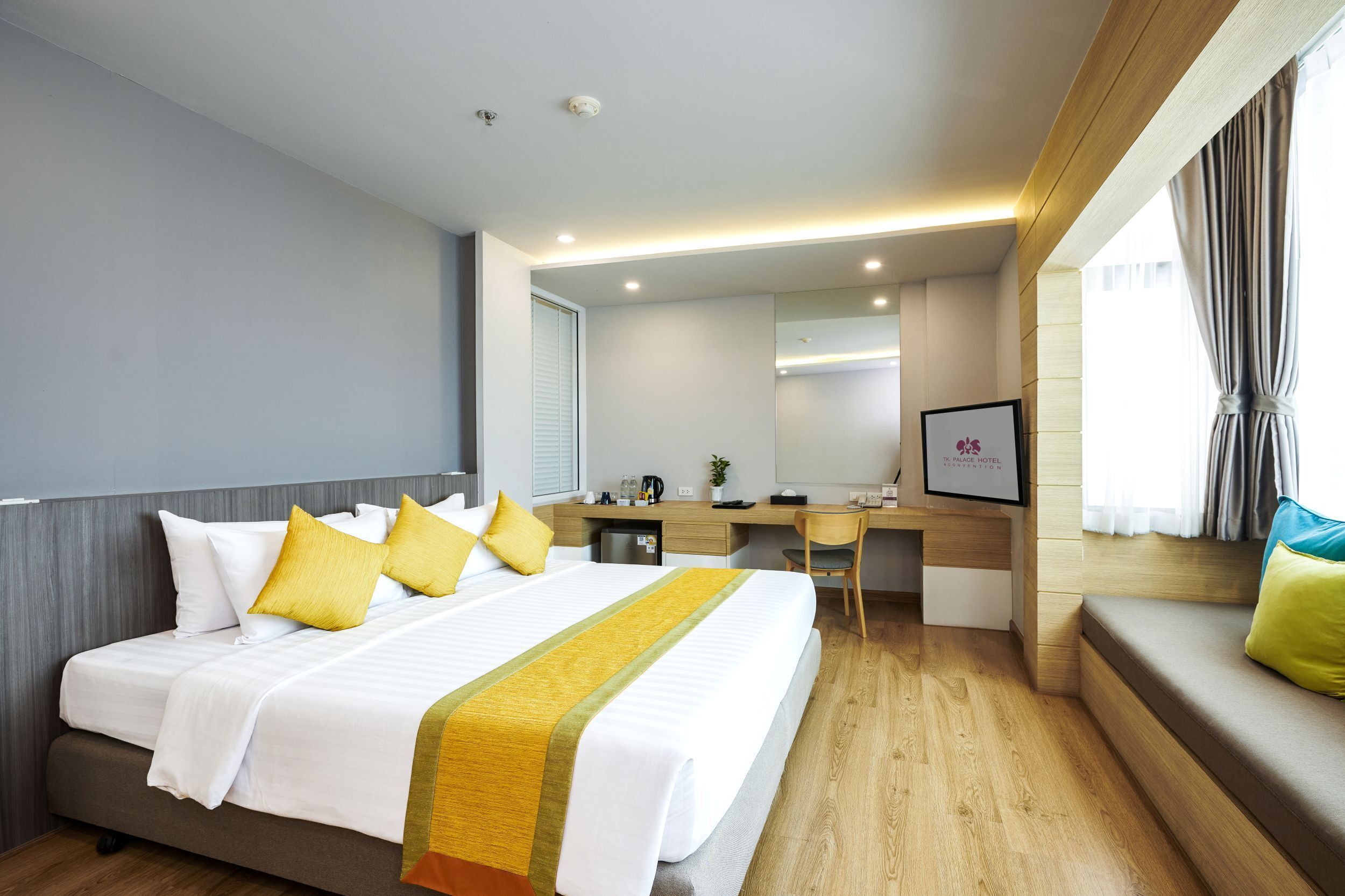 Una habitación de hotel con cama, escritorio, silla y ventana con cortinas.