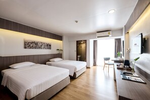 A hotel room with two beds, a desk with a computer, a flat-screen TV, and a cityscape artwork on the wall. - TK Palace Hotel & Convention (Bangkok)