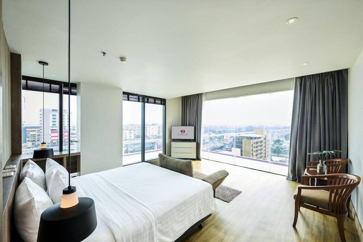 A modern hotel room with a large bed, a desk, a chair, a TV, and a view of the city.