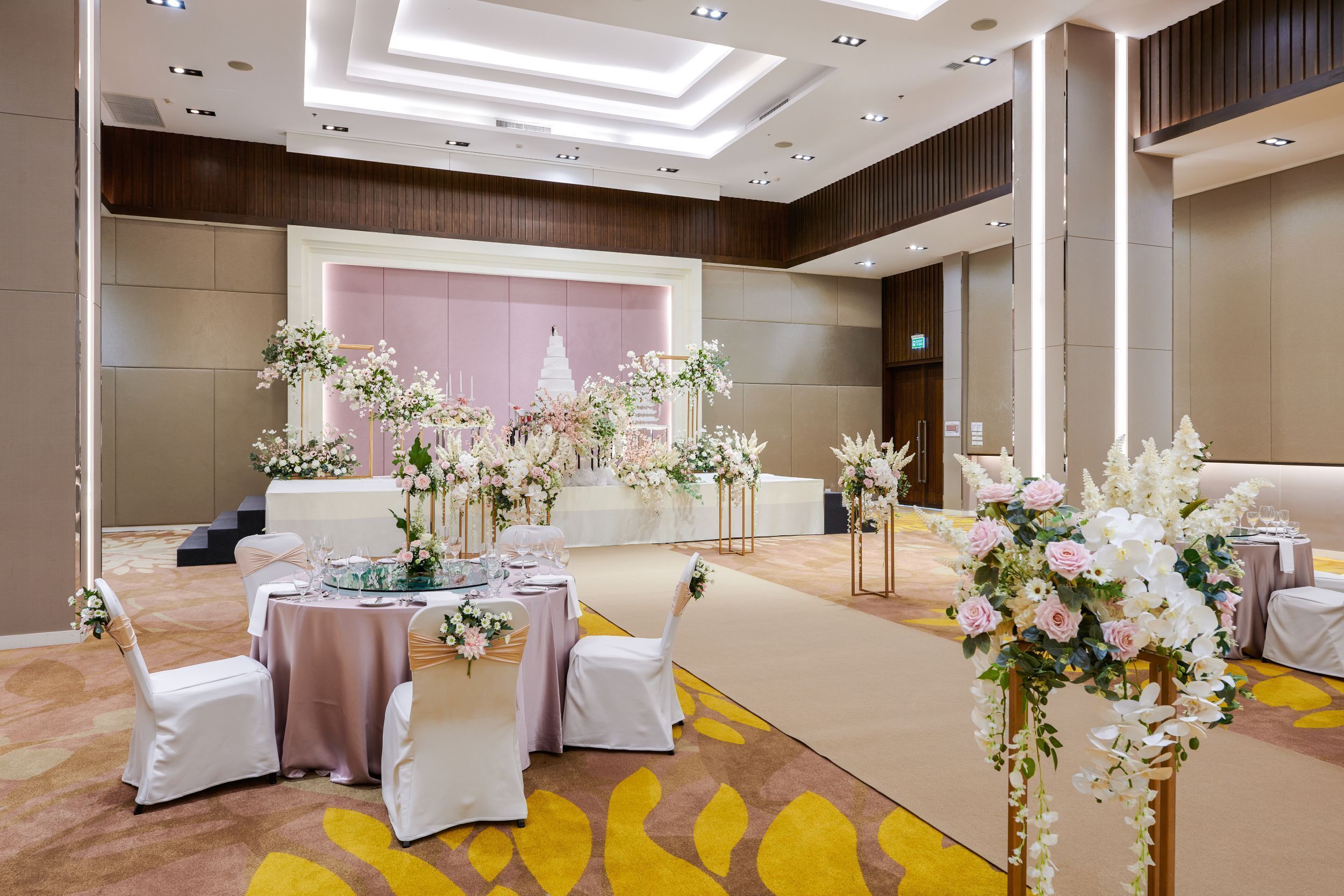 A banquet hall with round tables, white chairs, and floral centerpieces.