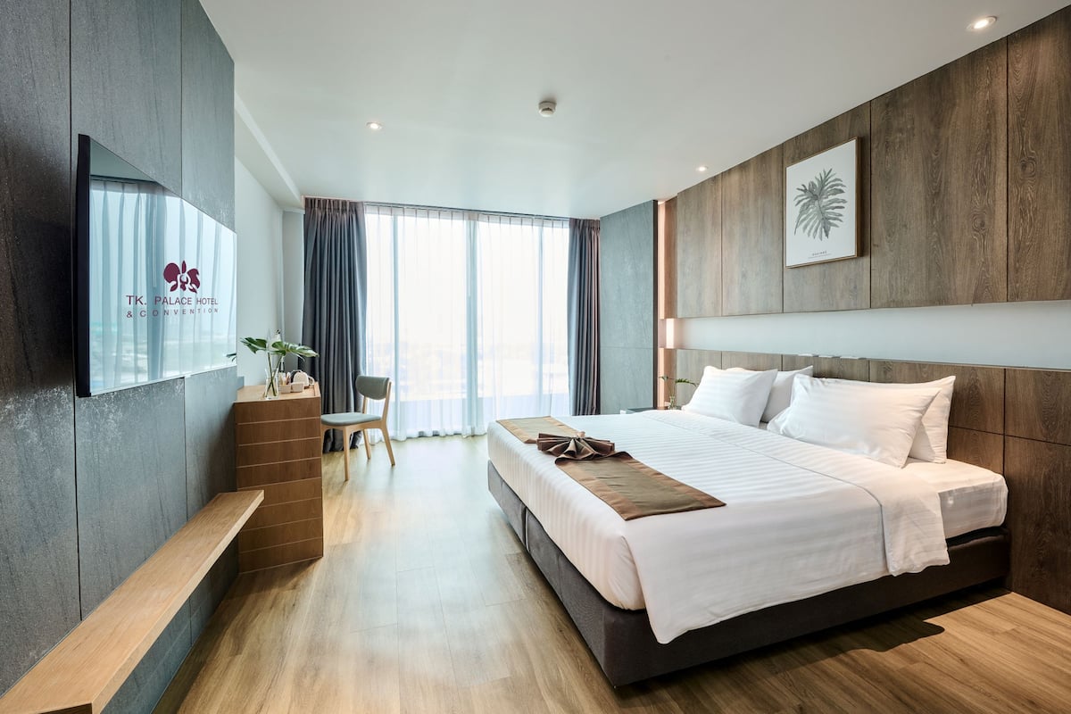A modern hotel room with a large bed, a wooden bench, a desk, and a TV on the wall.