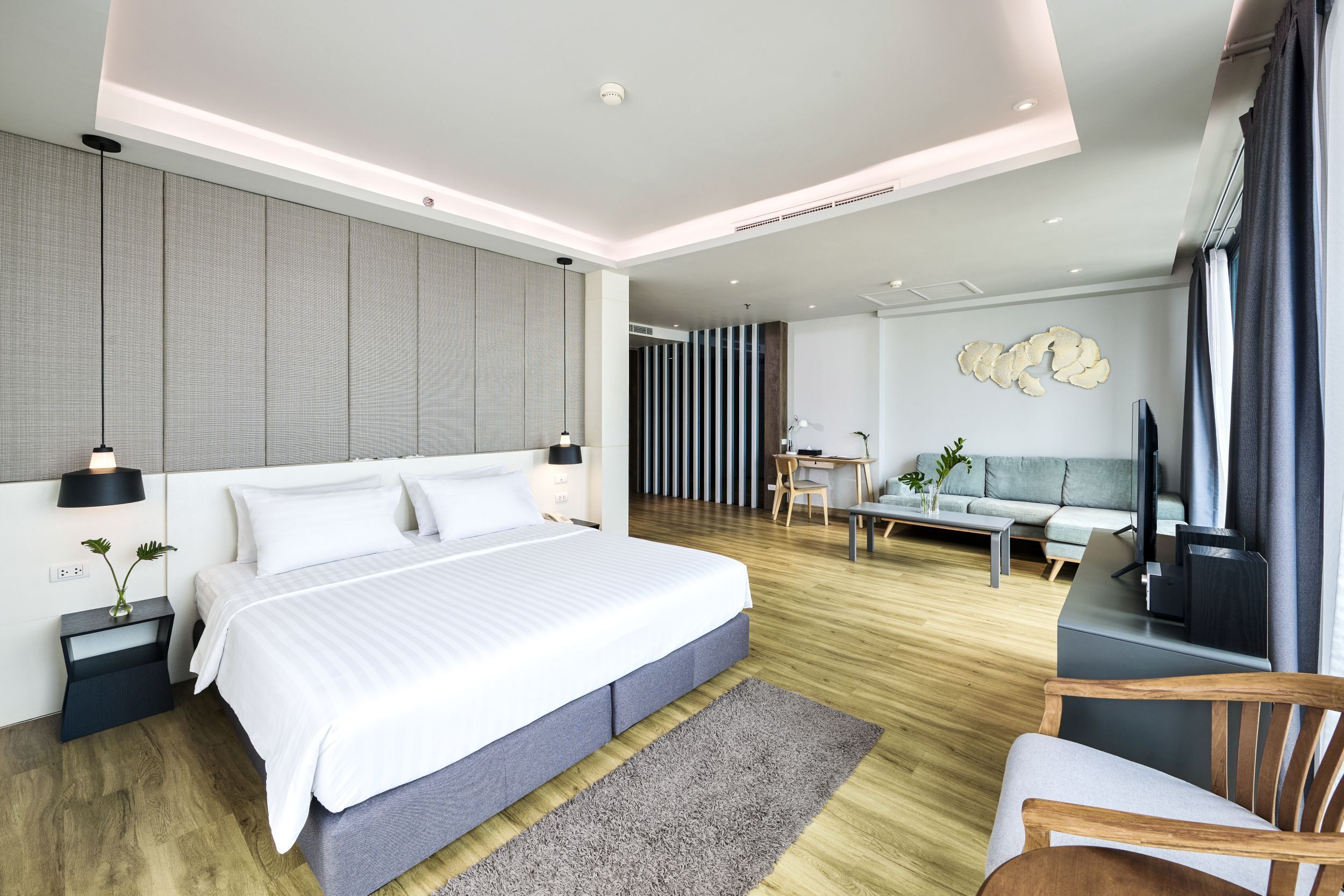 A modern hotel room with a large bed, a desk, a sofa, and a TV.