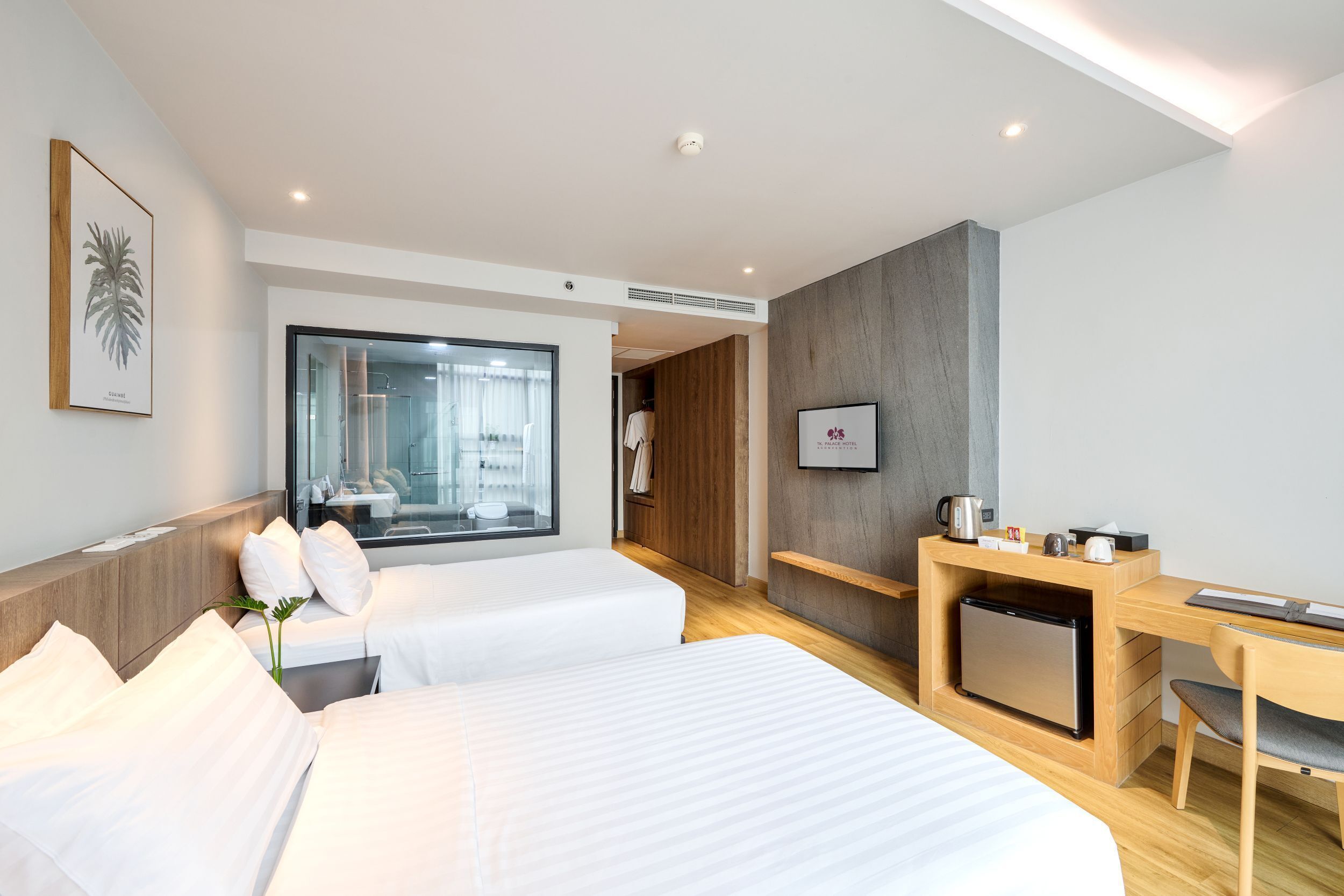 Une chambre d’hôtel moderne équipée de deux lits, d’un bureau, d’un petit réfrigérateur et d’une télévision.