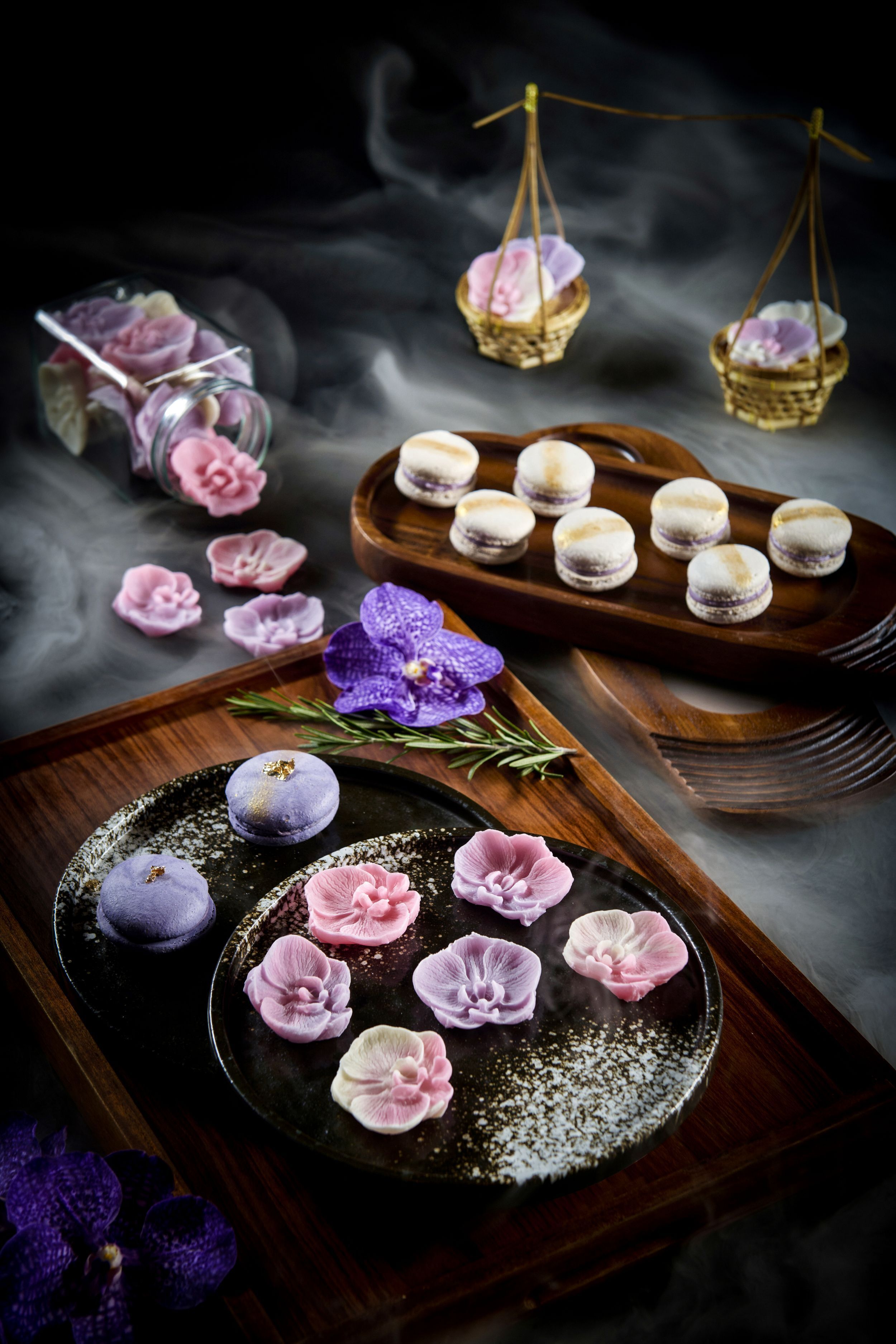 A dessert tray with macarons and flowers on a wooden board.