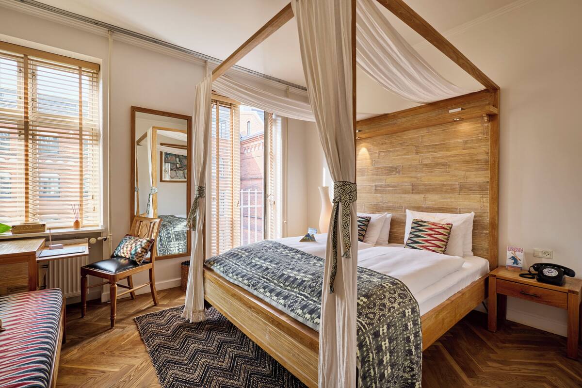 Un letto a baldacchino con tenda, una scrivania con sedia, un comodino con un telefono e vista sulla città attraverso ampie finestre.