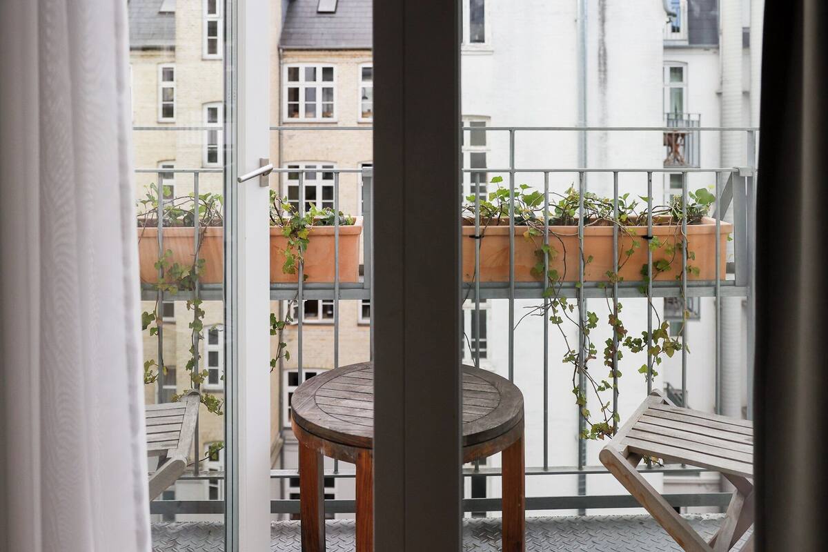 A balcony with a wooden chair, a small round table, and potted plants.