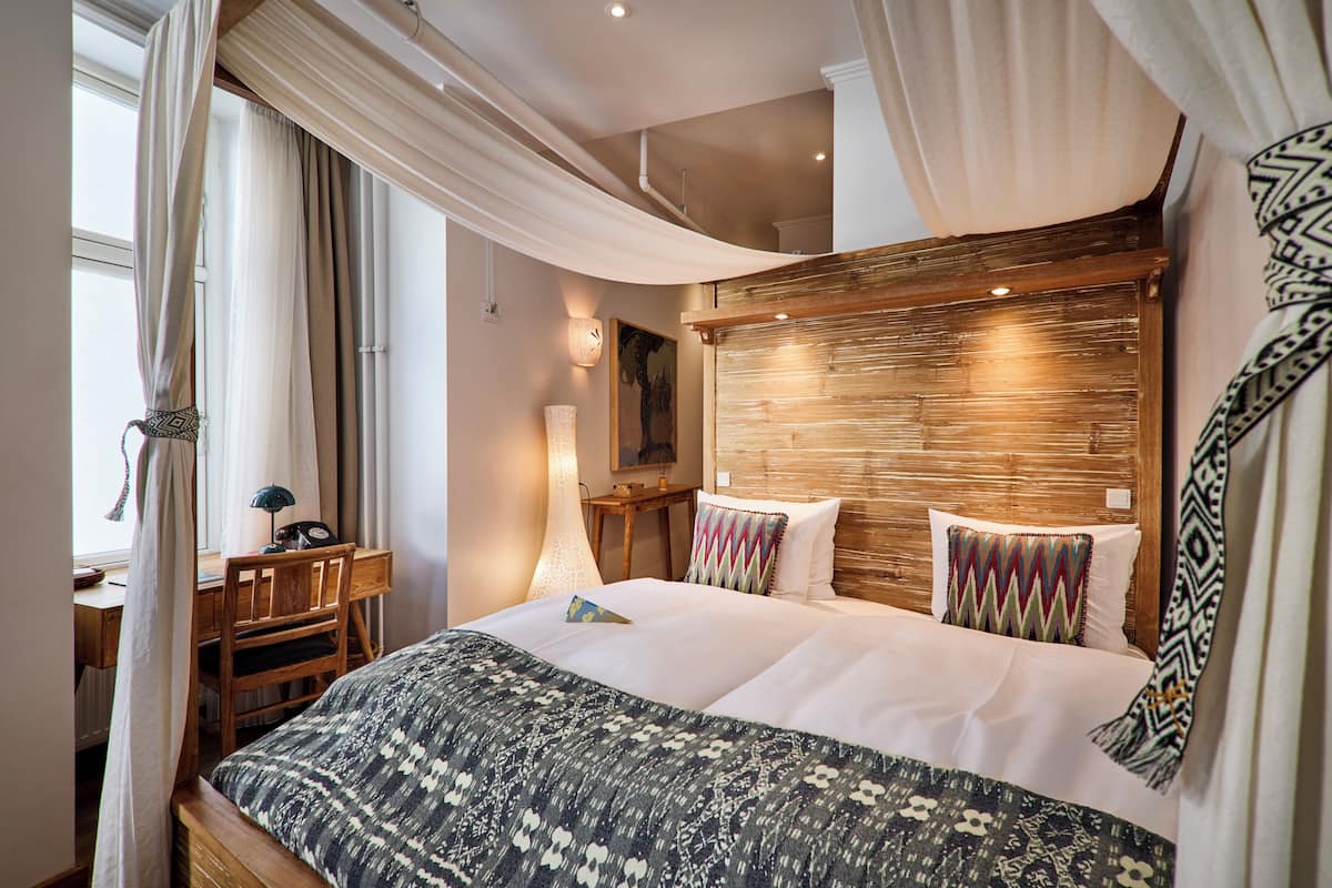 A bedroom with a large bed, a desk, a chair, and a lamp.
