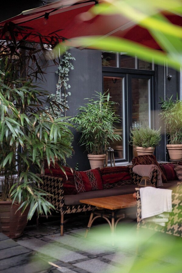An outdoor seating area with potted plants, a wooden bench, and a red umbrella. - Axel Guldsmeden  (Copenhagen)