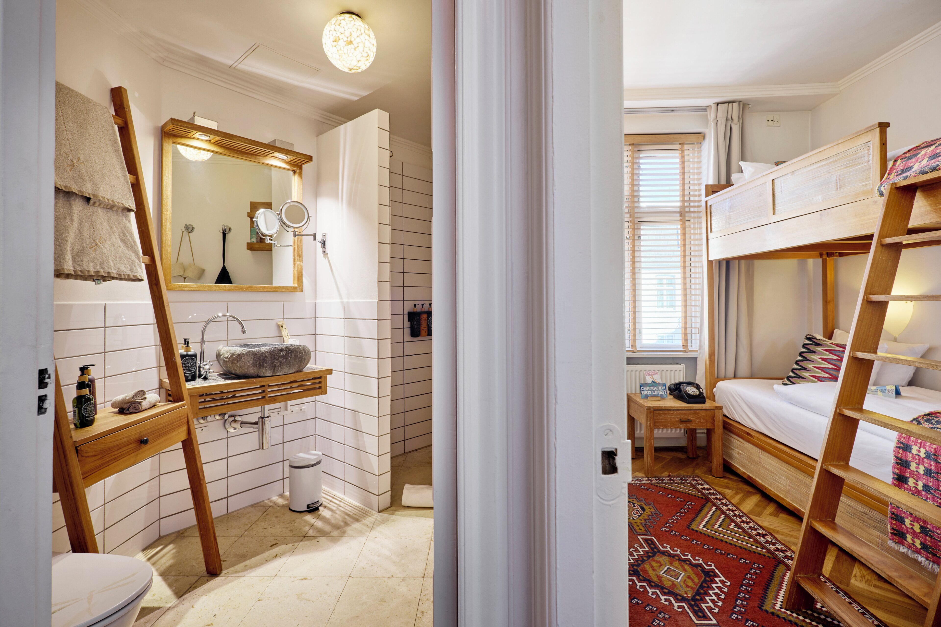 A compact room with a wooden bunk bed, a small bedside table, a mirror, and a sink with a towel rack.