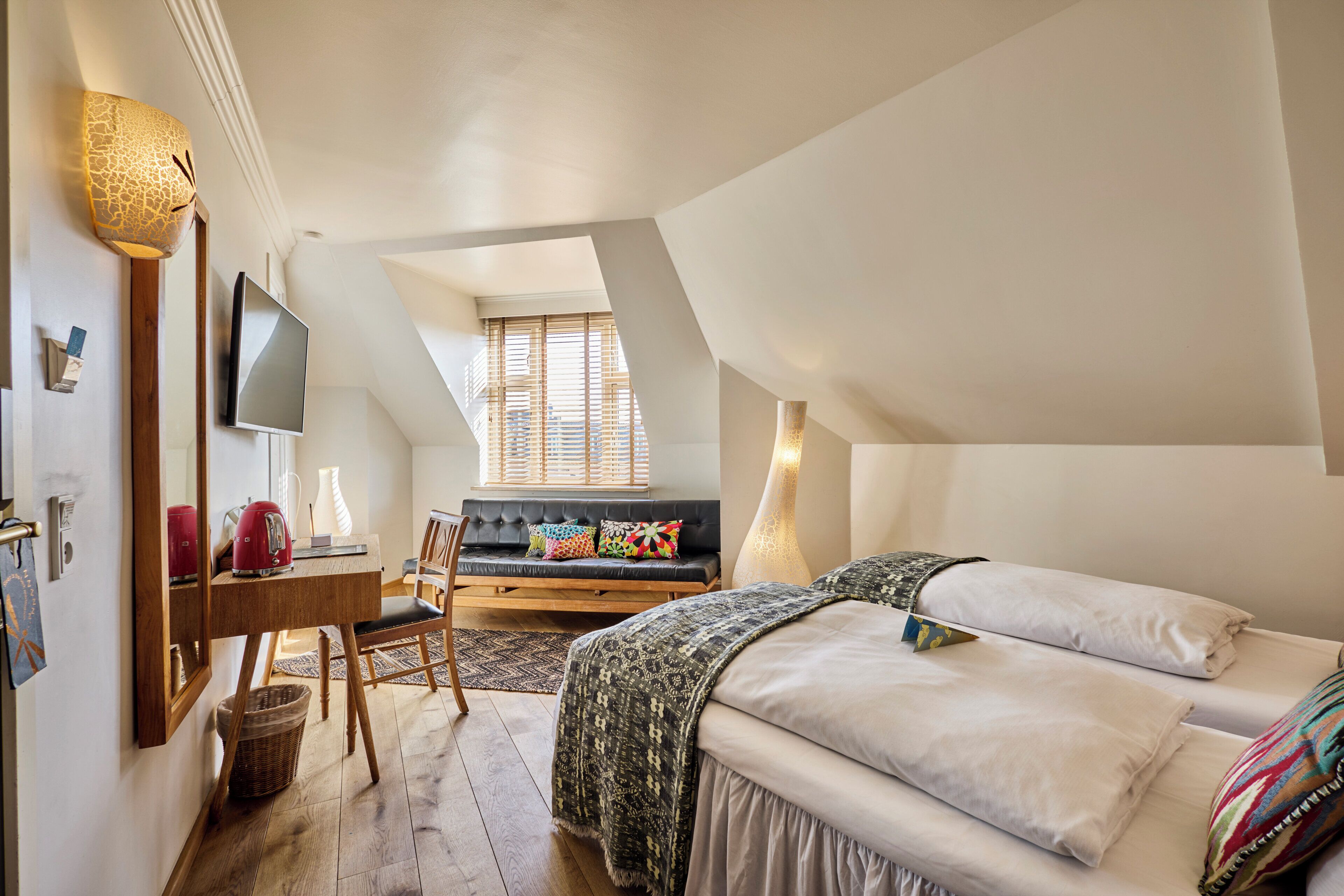 Un dormitorio con cama, escritorio, silla, televisor y ventana con persianas.