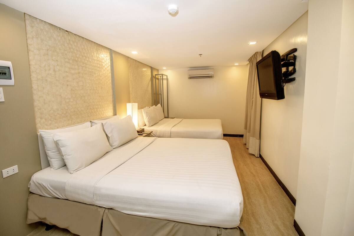 Une chambre d’hôtel avec deux lits, un appareil de climatisation, un téléviseur et un luminaire fixé au mur.