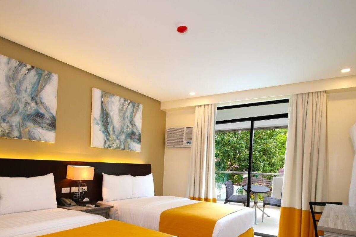 Une chambre d’hôtel avec deux lits, un balcon doté d’une table et de chaises, et des œuvres d’art accrochées aux murs.