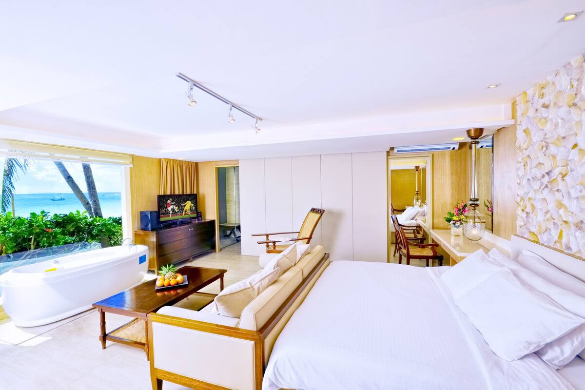 Une chambre d’hôtel moderne dotée d’un grand lit, d’un coin salon avec un téléviseur, d’un bureau et offrant une vue sur l’océan.