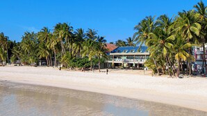 Un hotel frente a la playa con piscina, palmeras y una playa de arena.