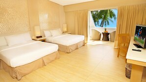 Habitación de hotel con dos camas, televisión, escritorio y vista a palmeras.