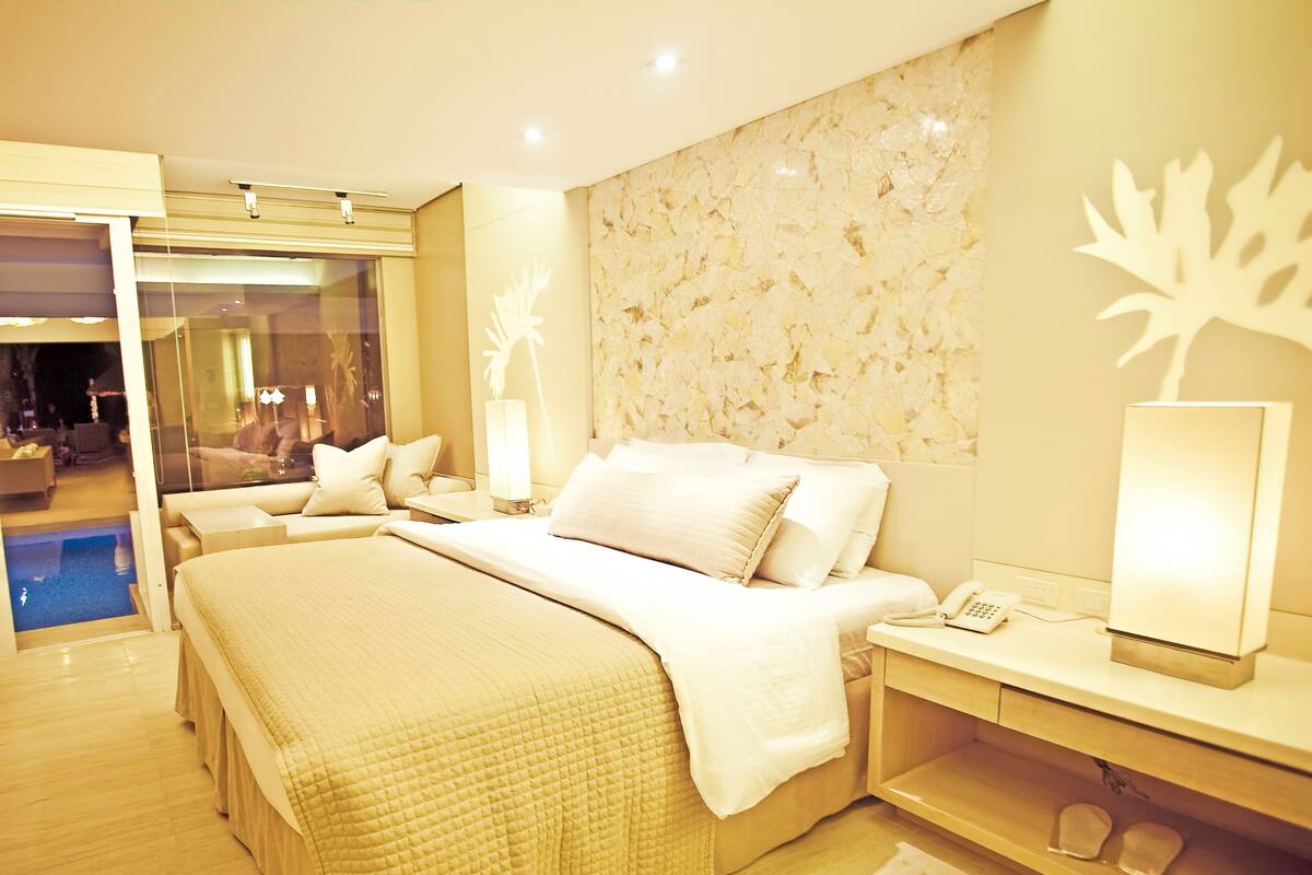 Une chambre d’hôtel moderne dotée d’un grand lit, de tables de chevet, d’un bureau intégré, d’un téléphone et offrant une vue sur l’espace piscine.