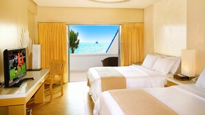 Habitación de hotel con dos camas, televisión, escritorio y ventana con vista al mar.