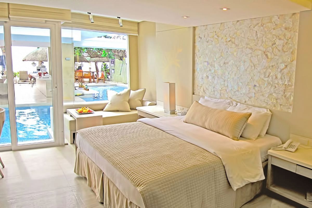 Een hotelkamer met een groot bed, een bureau, een stoel, een nachtkastje en uitzicht op een buitenzwembad.