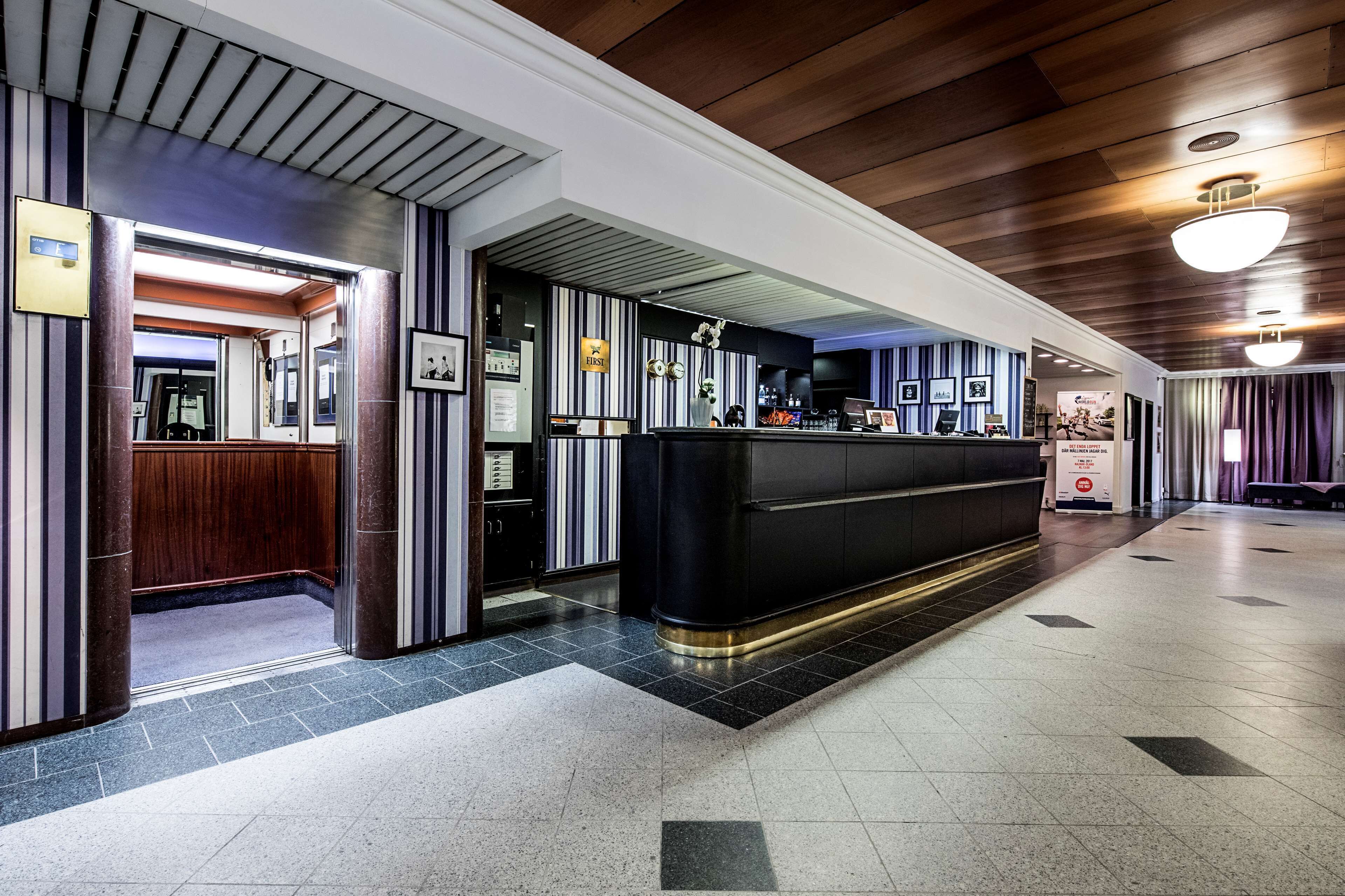 Un vestíbulo de hotel con una recepción, techo de madera y suelo de baldosas.