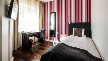 A hotel room with a bed, desk, chair, and a television.