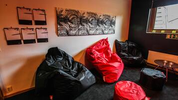 A room with a black and red bean bag, a black bean bag, a wall-mounted art piece, and a window with a view of buildings.