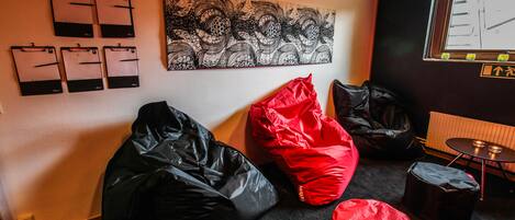 Una habitación con un sillón de saco negro y rojo, otro sillón de saco negro, una obra de arte colgada en la pared, y una ventana con vistas a edificios.