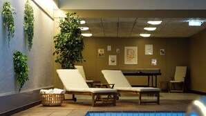 Un espace piscine aménagé avec des chaises longues, une table et des plantes fixées au mur.