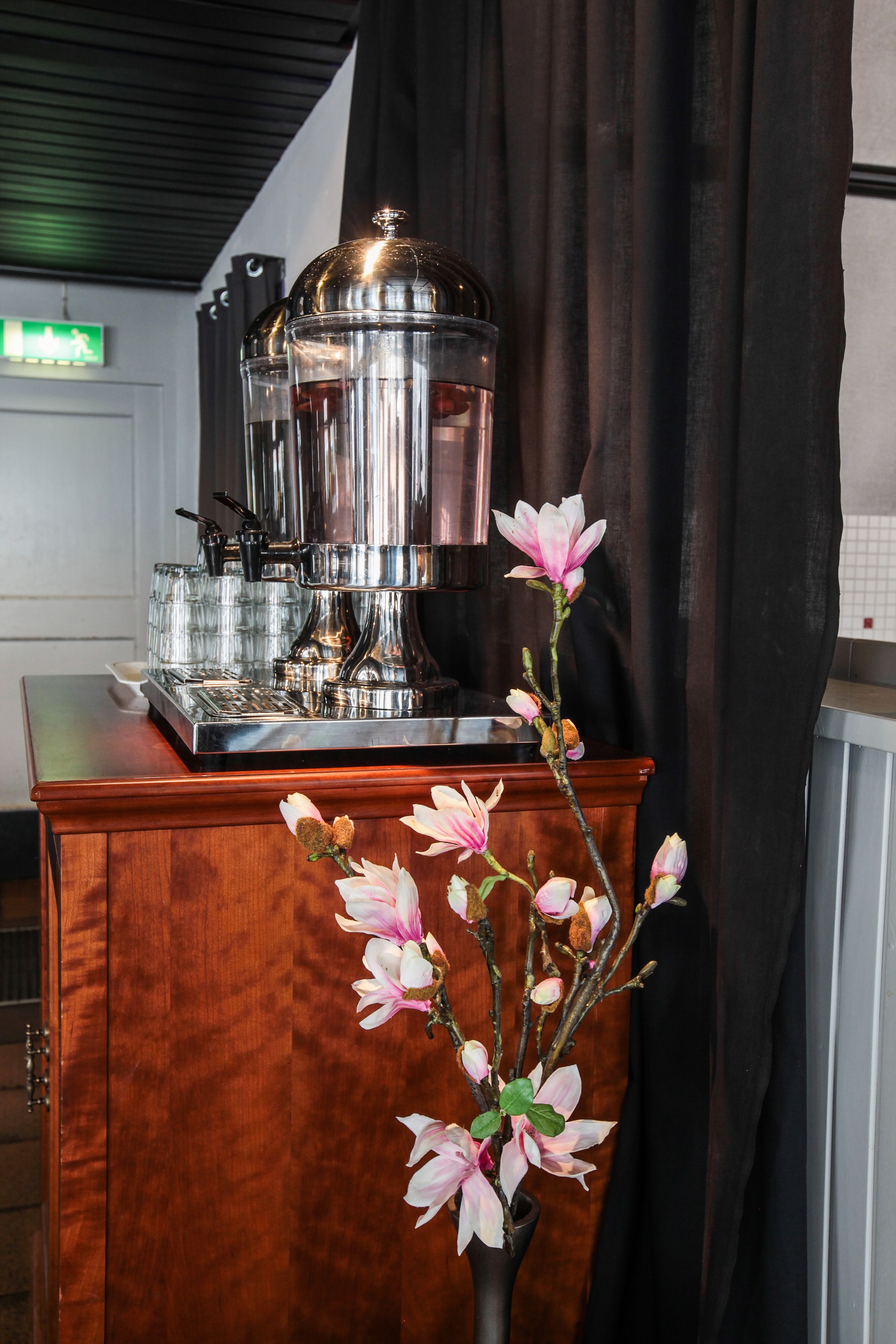 A coffee machine on a wooden counter with a vase of pink flowers.