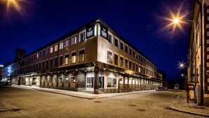 Un hôtel à plusieurs étages, reconnaissable à son grand panneau « First Hotel », doté d’un bar au rez-de-chaussée et d’une entrée bien éclairée.