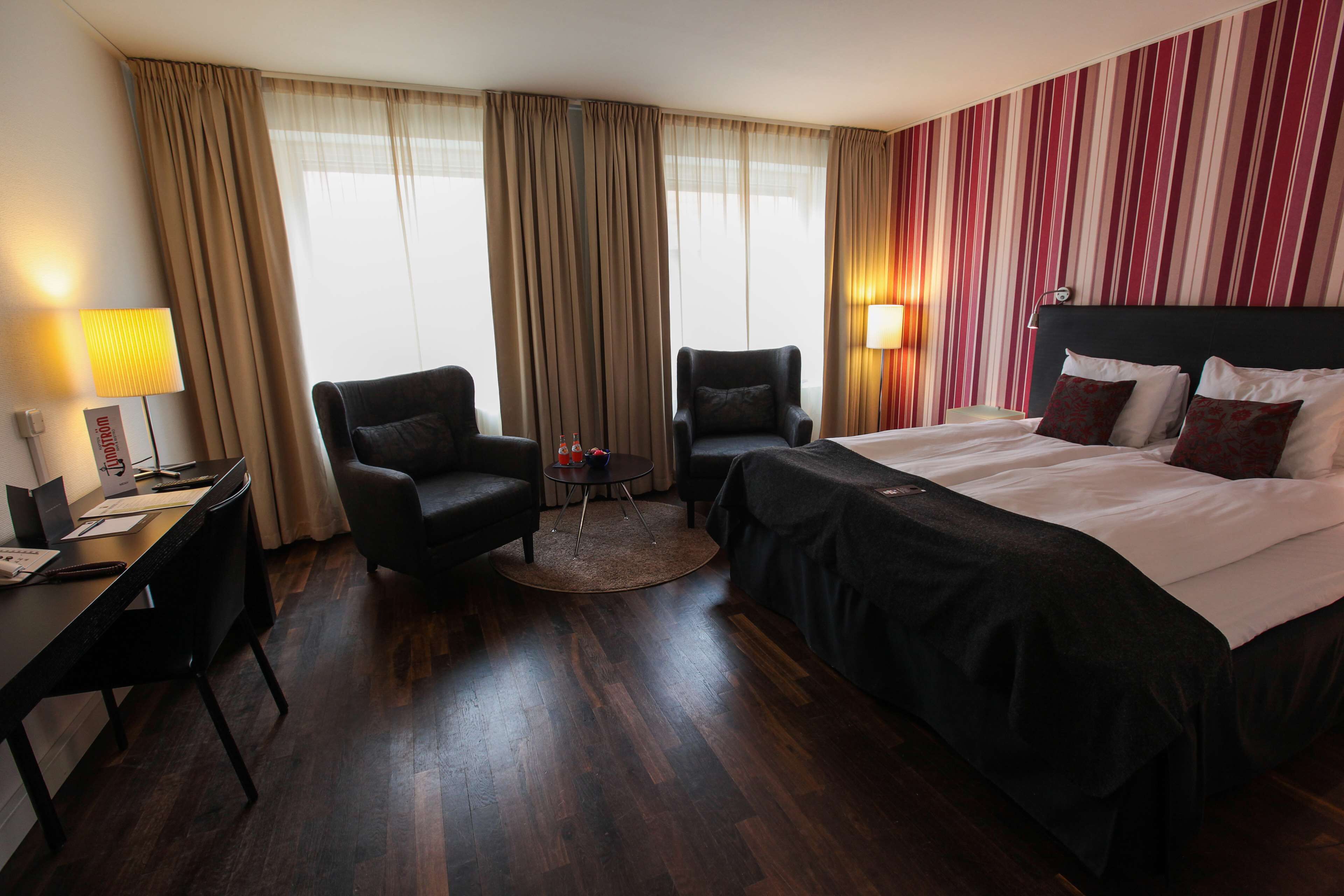 Una habitación de hotel con una cama, dos sillones, un escritorio y una mesita.