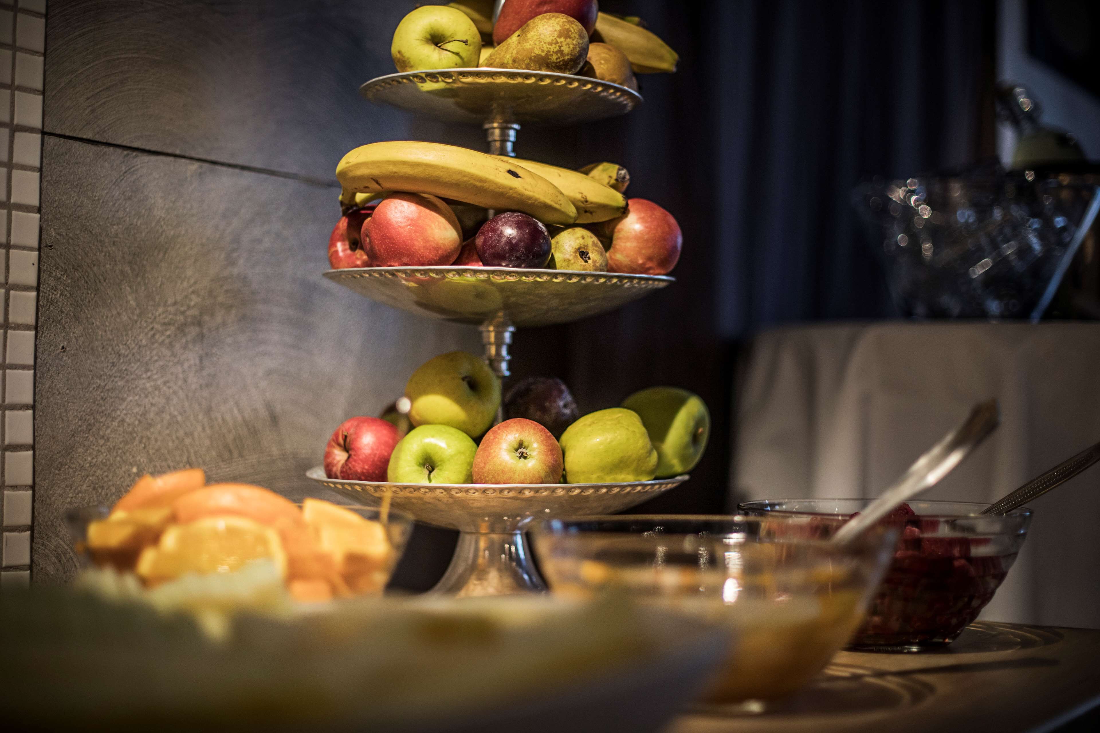 Une présentation de fruits comprenant des pommes, des bananes et des oranges, disposés sur un présentoir à plusieurs niveaux.