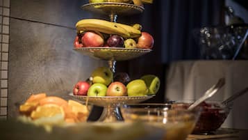 Una exhibición de frutas con manzanas, plátanos y naranjas sobre un soporte escalonado.