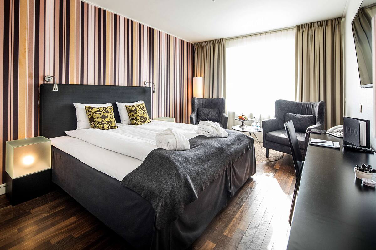 Una habitación de hotel con una cama grande, dos sillones, un escritorio y un televisor.