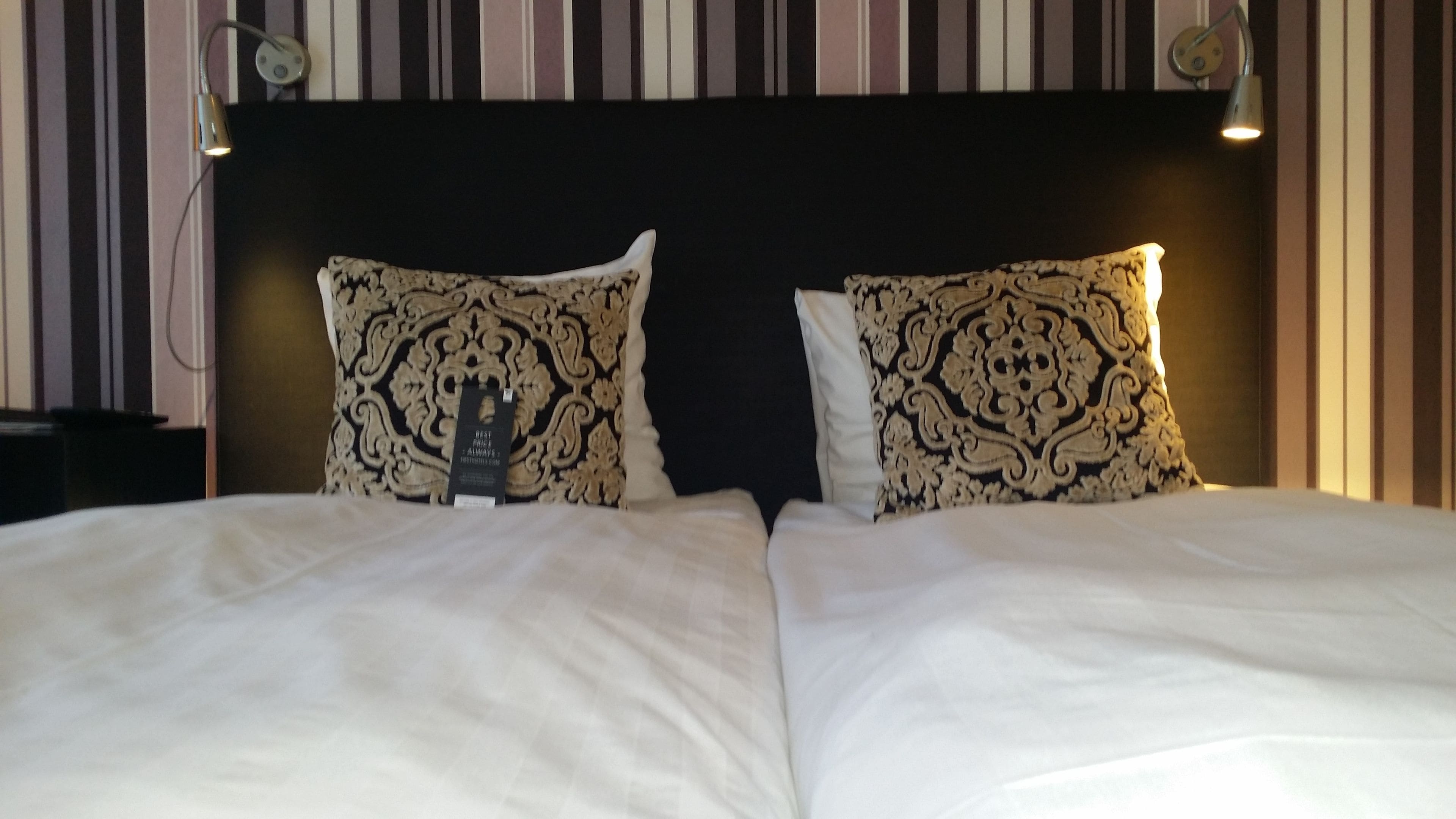 Un lit bien fait, agrémenté de deux coussins décoratifs et d’une étiquette fixée à la tête de lit.