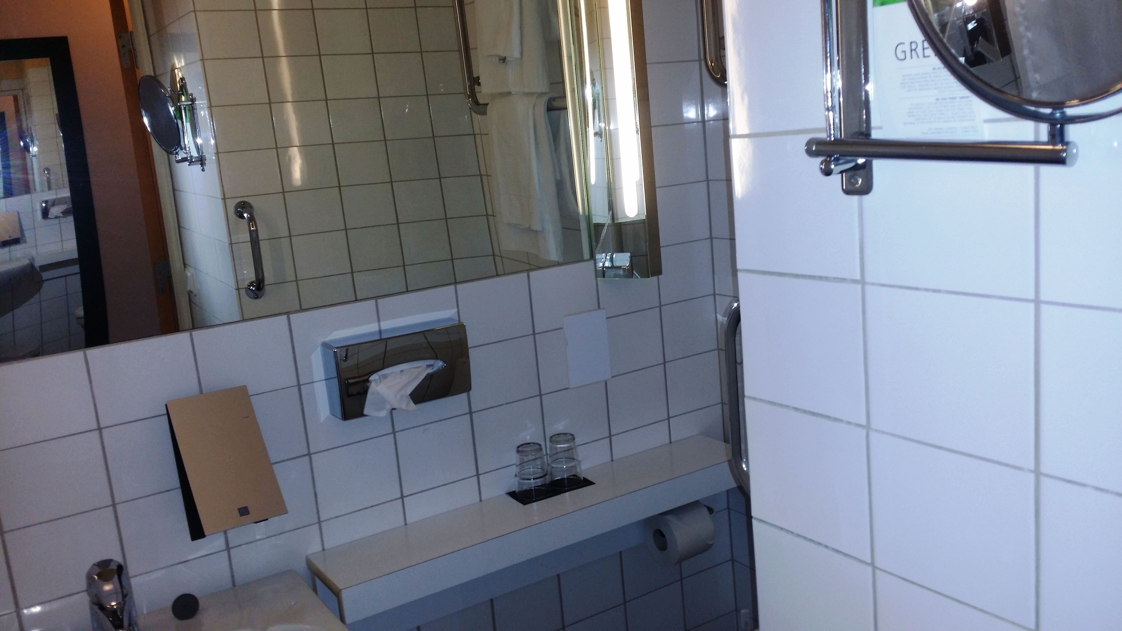 A bathroom with a mirror, a towel dispenser, a soap dispenser, and a toilet paper holder.